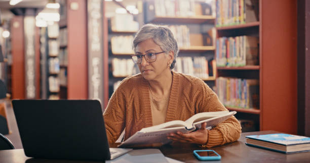 femme âgée, ordinateur et planification dans une bibliothèque avec livre et ordinateur portable pour le cours magistral. enseignant, professeur d’université et travailleur de l’éducation lisant des données web et effectuant des recherches pour la - professeur duniversité photos et images de collection