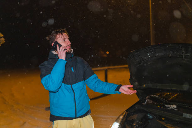 istock Stressed young man talking on the phone while standing in front of his stuck car 1460019678