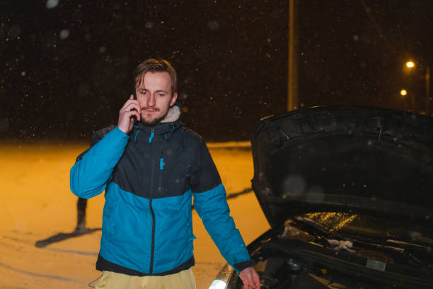 istock Stressed young man talking on the phone while standing in front of his stuck car 1460020205