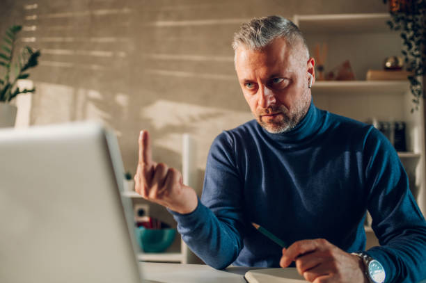 istock Middle aged man showing middle finger to a laptop screen while working at home 1460020383
