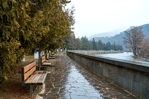 Walking alley with benches along the river with a picturesque view of the mountains.