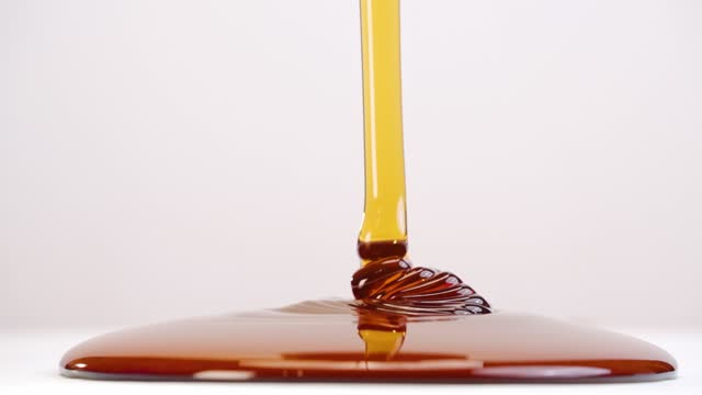 Glob of honey drizzled onto white plate stacking ripples in slow motion back and forth on white studio backdrop in 4k