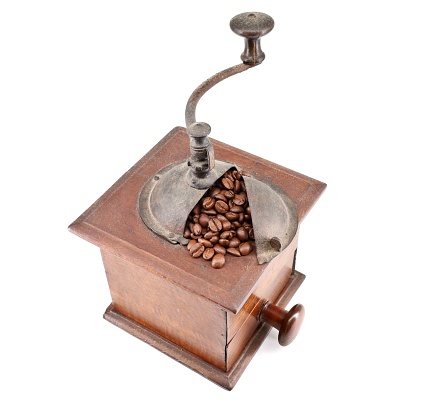 Old manual coffee grinder. Brick wall as a background with scattered coffee beans on the table