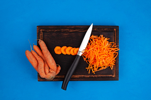 Deformed conjoined carrot and knife on cutting board, top view. Ugly vegetable abnormal shape. Curved funny carrots. Concept - Food waste reduction. Using in cooking imperfect products.