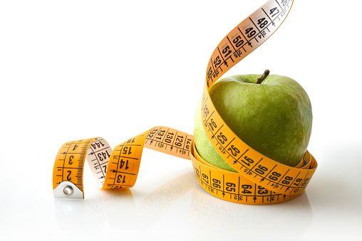 Apple rolled by a tape measure reflected on white base and white isolated background. Healthy life style. Front view.
