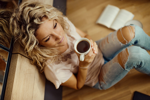 High angle view of young woman relaxing during coffee time on floor at home.