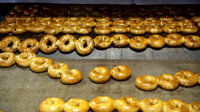 Making of the fresh hot tasty bagels at the backery's factory: bagels comes out from the oven