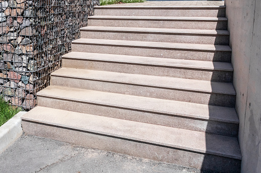 Stone staircase with massive steps made of polished stone slabs in a landscaped garden.