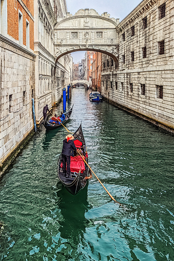 Photo of a canal flowing under the Bridge of Sighs in Venice, Italy, with a rear view of Gondoliers in the distance