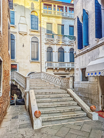 Photo of a marble steps leading to a bridge crossing a canal in Venice, Italy, with surrounding architecture