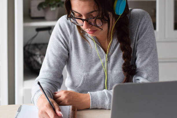 istock Young girl student in headphones writing notes while studying at home 1460033555