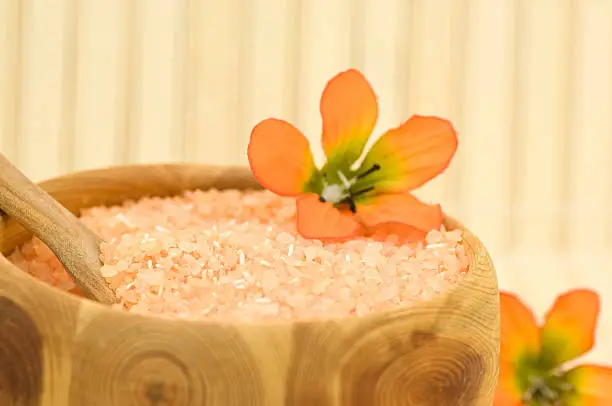 Close up on aromatic bath salt with decoration flowers on bamboo, focus on bath salt at the spoon