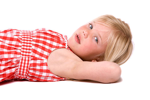 Sexy young girl dressed in pink dress and holding a hat while lying down on green grass.