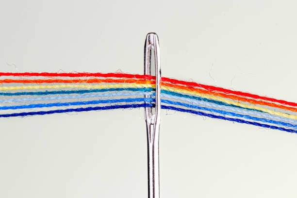 multi-colored threads for sewing in the form of a rainbow pass through an antique needle on a white background close-up