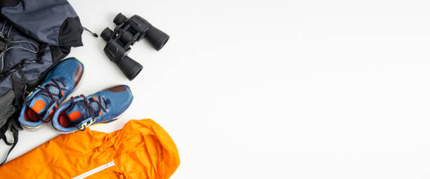 istock Binoculars, tourist backpack, raincoat, shoes on a white background. Top view, flat lay. Banner 1460041012
