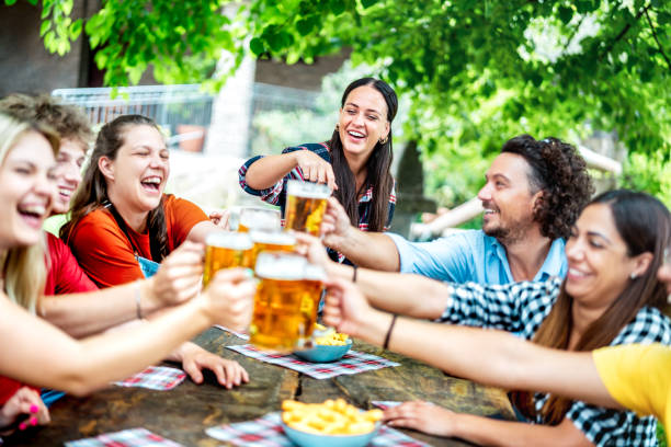 Young friends drinking and toasting beer at brewery bar restaurant - Beverage life style concept with happy guy and girls having fun together out side - Bright vivid filter with focus on mid woman stock photo