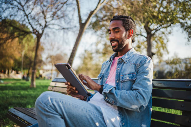istock Young man sitting on a park bench with digital tablet 1460046588