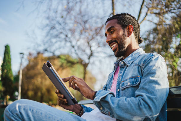 istock Young man sitting on a park bench with digital tablet 1460046601