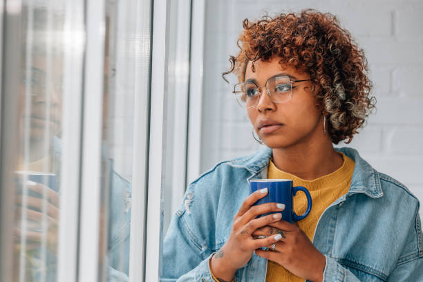 istock pensive woman at home looking out the window with cup 1460049310