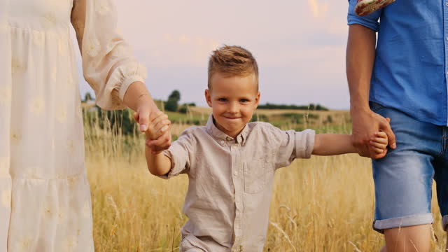 Slow motion tracking shot of a family of four, walking down a gold coloured meadow