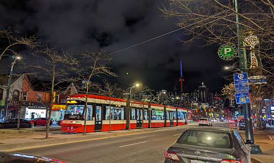 Toronto, Canada - December 9, 2022: A TTC 510 Spadina streetcar heads north on the 300-block of Spadina Avenue at Baldwin Street. Night lights shine in the Kensington-Chinatown neighbourhood of downtown. Background shows the CN Tower and the upscale residential district.
