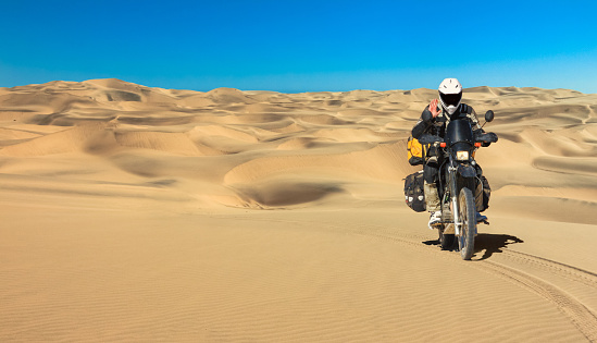 Lonely Motorbiker driving in sand dune desert. Motorcycle Expedition in Namib Desert, Namibia
