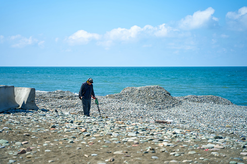 A man with a metal detector is looking for jewelry lost by vacationers on the beach. Batumi, Georgia - 03.30.2021