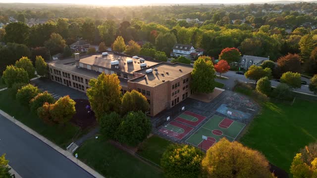 Small town in USA. School building with recess playground. Aerial in autumn. Golden hour light.