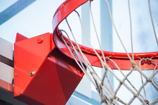 A view of the metal hinge of a basketball hoop and background at an outdoor park.