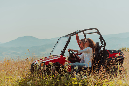 Two young happy excited women enjoying beautiful sunny day while driving a off road buggy car on mountain nature.