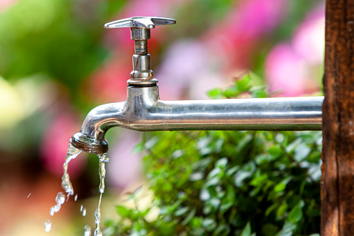 Iron shiny brazilian faucet leaking clean water. Garden backyard blurry background