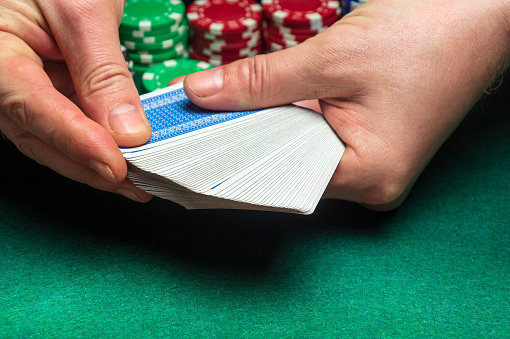 Close-up hands of a person-dealer or croupier shuffling poker cards in a poker club on the background of a table, chips. Poker game or gaming business concept