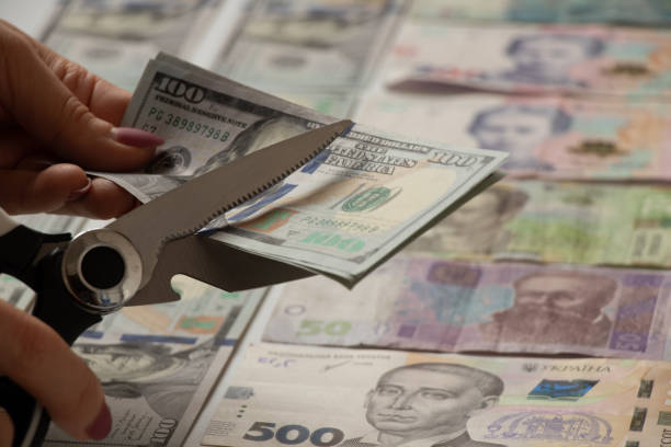 ドルとウクライナのグリブナは白い背景にあり、女性の手はハサミ、ビジネスと経済を背景に、危機と借金で100ドルを切ります - currency paper currency wealth one hundred dollar bill ストックフォトと画像