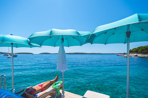 Woman on a sun lounge at the beach. Crystal clear turquoise water can be seen.