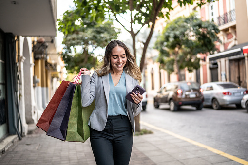 Mid adult businesswoman using phone and carrying shopping bags outdoors