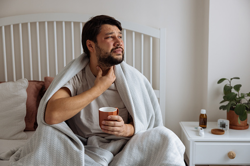 Man blowing his nose while lying sick in bed