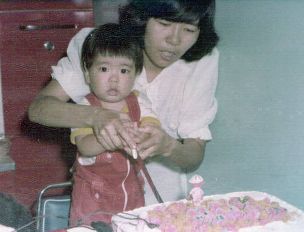 Young mother with her baby son celebrating his first birthday Young mother with her baby son celebrating his first birthday. This is a digitized old family picture 70s birthday party cake stock pictures, royalty-free photos & images