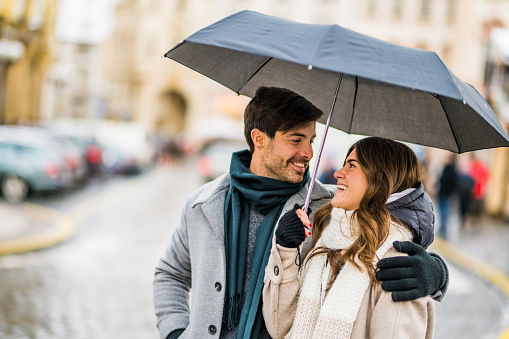 Charming couple walking outdoors in the city together on a rainy winter day.