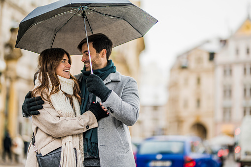 Romantic couple embracing and walking on city street with an umbrella on a rainy winter day.