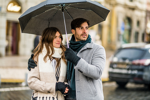 Elegant couple walking on city street with an umbrella on a rainy winter day.