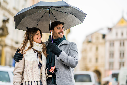 Young couple in love with umbrella stroll through the city in rainy weather