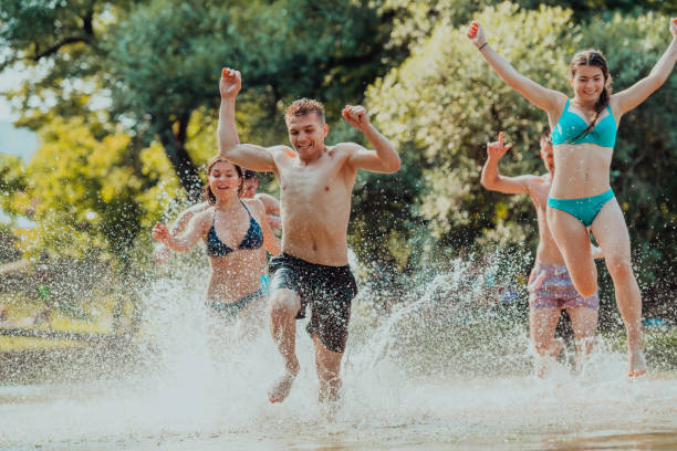 un gruppo di giovani eterogenei che si divertono insieme mentre corrono lungo il fiume e giocano a giochi d'acqua - men beach running shirtless foto e immagini stock