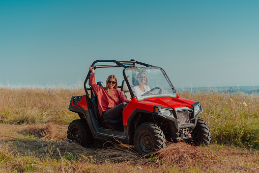 Two young happy excited women enjoying beautiful sunny day while driving a off road buggy car on mountain nature.