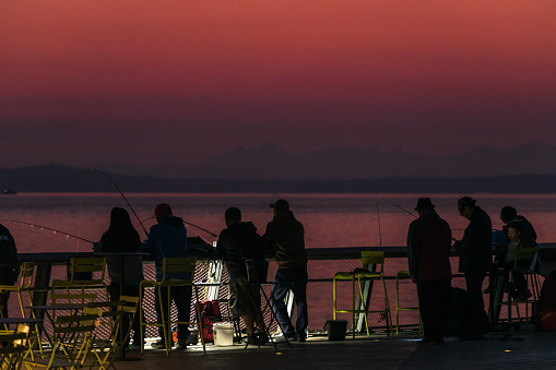 Seattle, USA - Oct 9th, 2022: A vivid sunset on Elliott bay off pier 62 as people fish in the unusually warm weather.