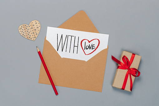 Flat lay composition of craft paper envelope and white card with hand written St. Valentines day greetings and love confession, isolated on grey background.