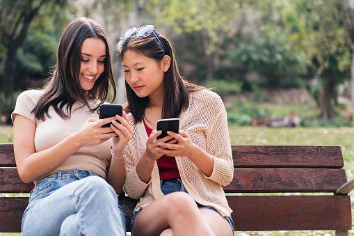 two young women smiling happy while looking their mobile phones, concept of youth and communication, copy space for text