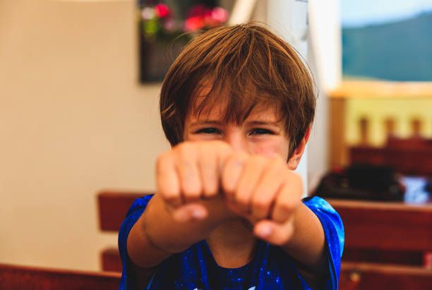 Portrait of boy acting dangerous and squinting eyes, crossing arms and showing fists straight to camera