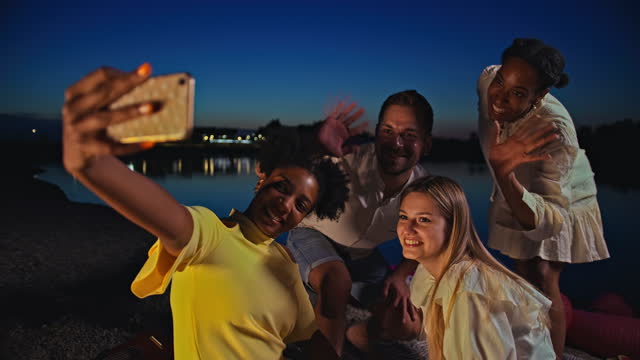 SLO MO Four people waves at the camera while they pose for a selfie on the beach at dusk