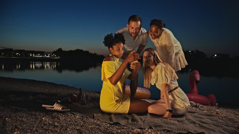 SLO MO Four young friends looks at the screen of a smartphone on the beach at dusk