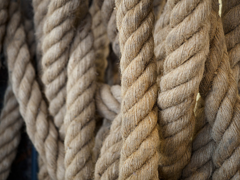 The image captures the essence of seamanship through the hands of a sailor as she firmly holds onto a robust, neatly coiled ship's rope. The thick fibers, woven with precision, are a testament to the durability and strength required for life at sea. The sailor's beaded bracelets add a personal and colorful touch to her practical grey dress with black lace detailing at the waist, marrying her seafaring role with a sense of individuality and grace.